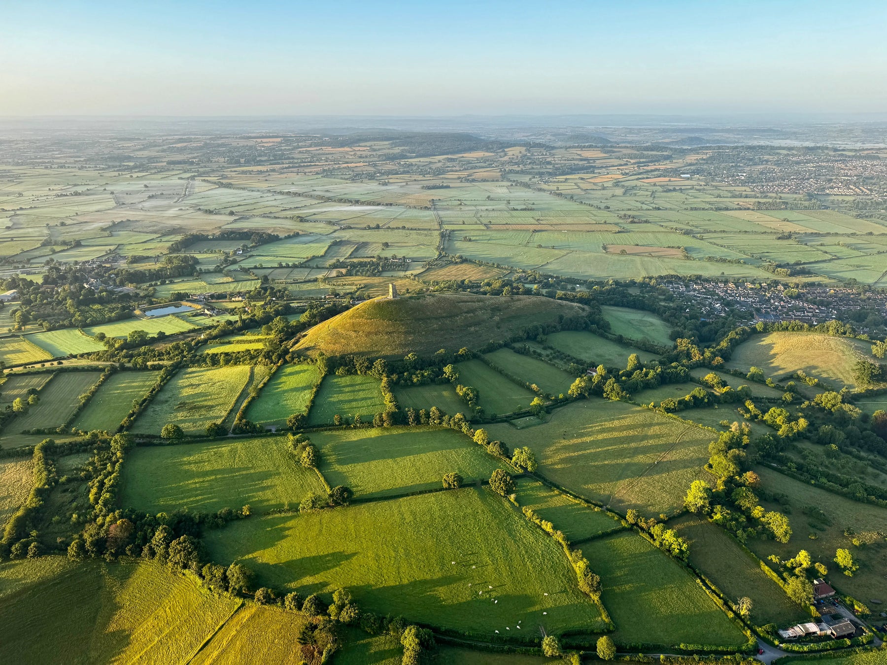 Glastonbury Tor rising above morning mist with patchwork Somerset fields viewed from a hot air balloon