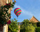 Colourful hot air balloon soaring above a charming garden in a Somerset village near Taunton, on a clear morning. A picturesque and peaceful start to a Taunton balloon ride. 