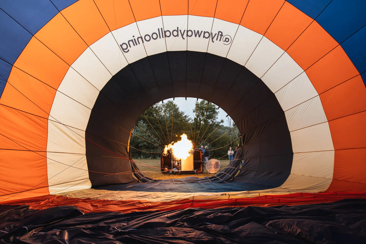 The inside of a Fly Away Ballooning hot air balloon being inflated with a burner before takeoff, showing the orange, white, and blue panels.