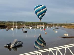 hot air balloon floating over a calm marina at Topsham, Devon with boats and reflections in the water during a morning balloon ride.