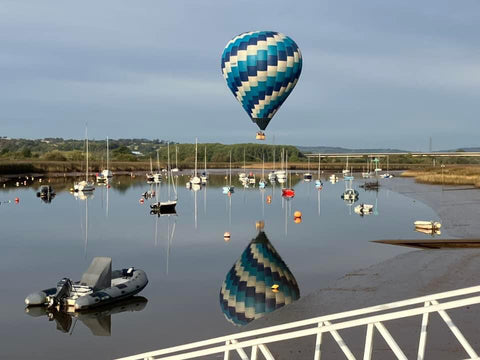 hot air balloon floating over a calm marina at Topsham, Devon with boats and reflections in the water during a morning balloon ride.