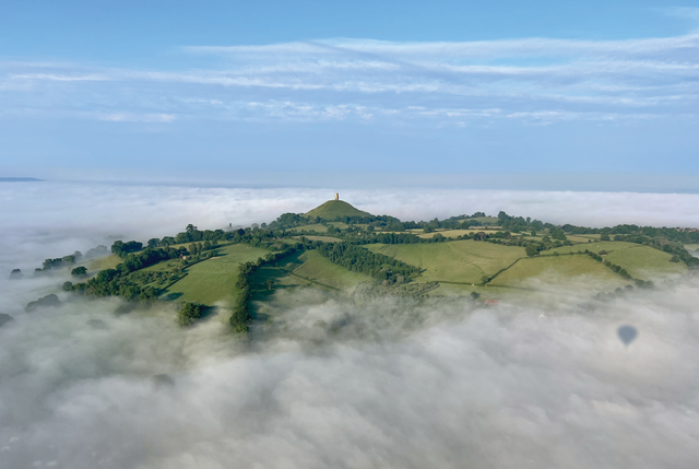 Aerial view of Glastonbury Tor rising above the morning mist during a scenic Glastonbury balloon ride over the Somerset countryside.