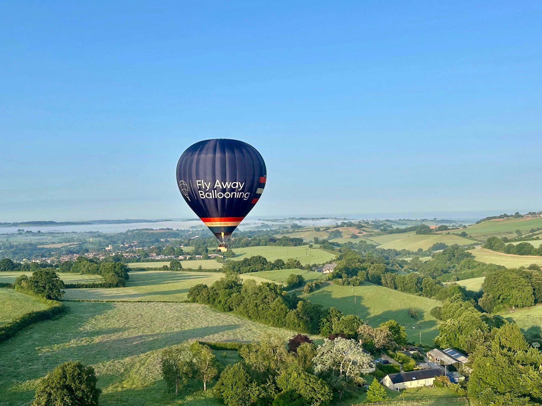 Fly Away Ballooning hot air balloon flying over countryside near Wells in Somerset on a clear morning