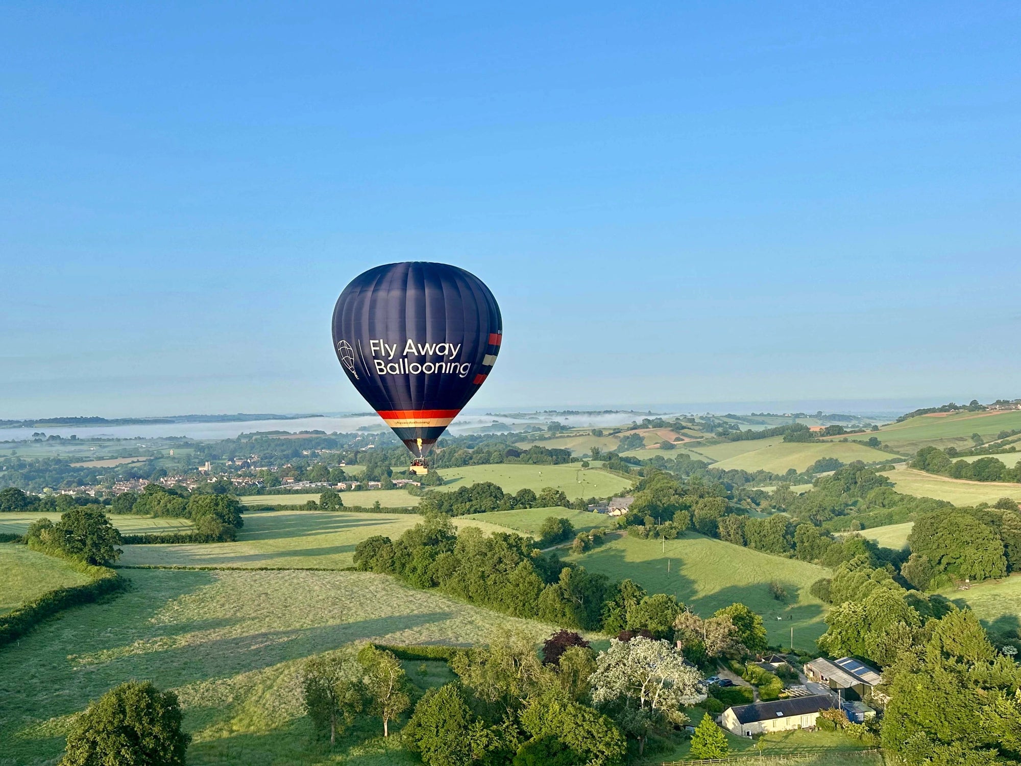 Fly Away Ballooning hot air balloon flying over countryside near Wells in Somerset on a clear morning