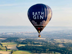 Bath Gin hot air balloon floating above the patchwork fields and coastline of Somerset during a clear morning flight - offering breathtaking views on a Somerset hot air balloon ride.
